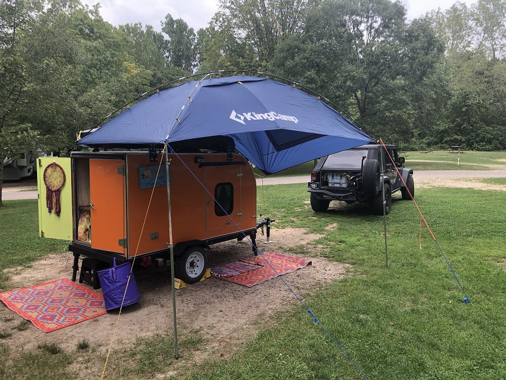 An orange squaredrop camper with a blue awning.