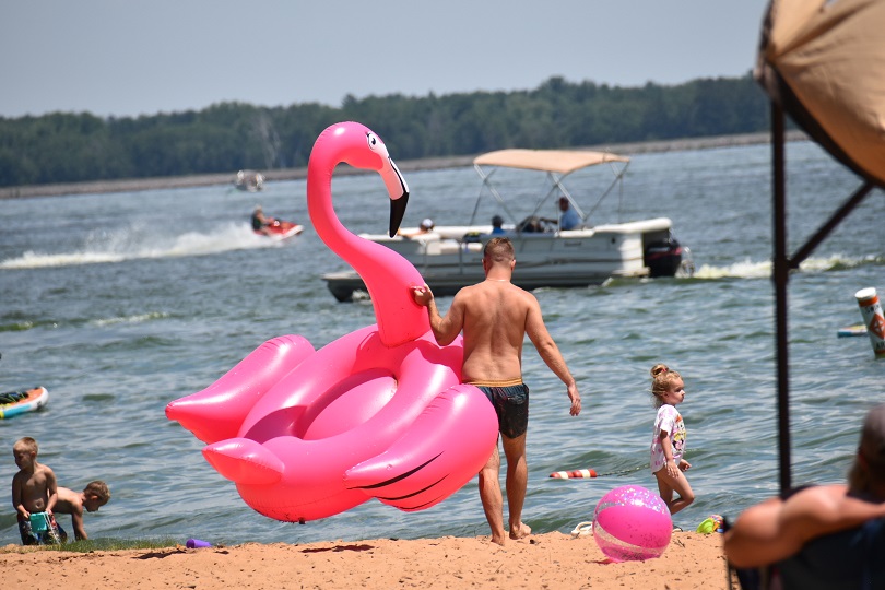 Man on the beach carrying a huge inflatable pink flamingo floaty