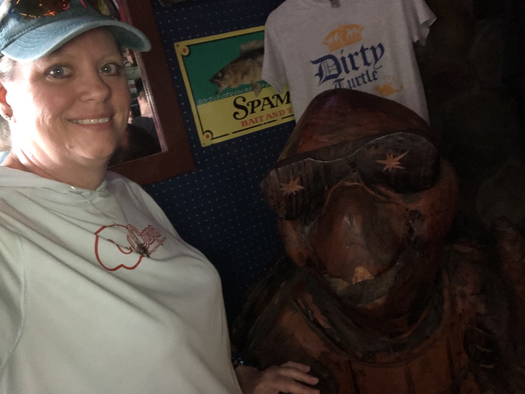 Woman in a baseball cap posing with a carved wooden turtle statue