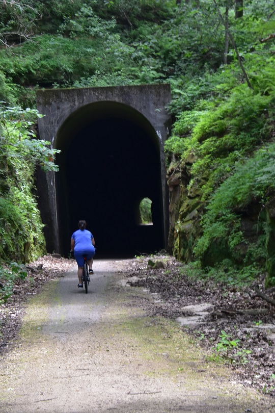 Woman on a bicycle riding into old railway tunnel with light at the end