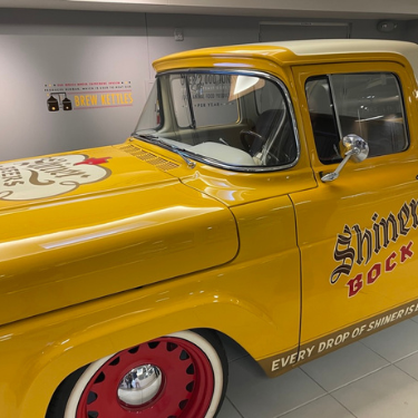 A reburbished old Ford Truck painted Shiner yellow with the logo for Shiner Bock on the sides and on the hood.  The tires wells are red and the trim is leather inside.