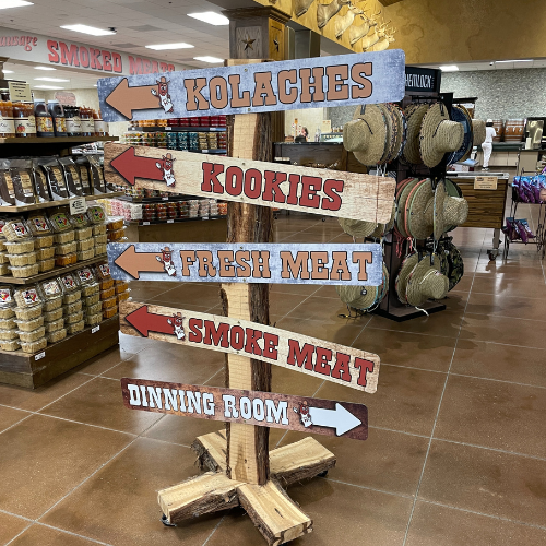 Directional signs on a tall post with the arrows pointing to different parts of Prasek's store.  Kolaches, cookies, fresh meat, smoked, meat, and dining room.