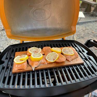 On open tabletop grill with cedar planked salmon cooking
