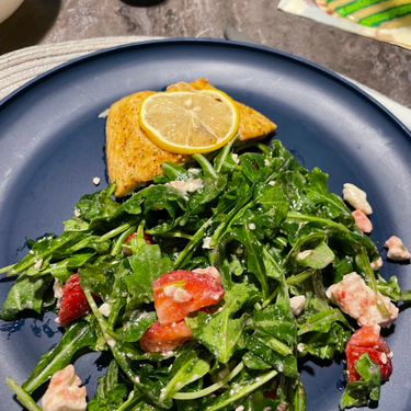 a blue plate is filled with cedar planked salmon and arugala salad with feta cheese and watermelon