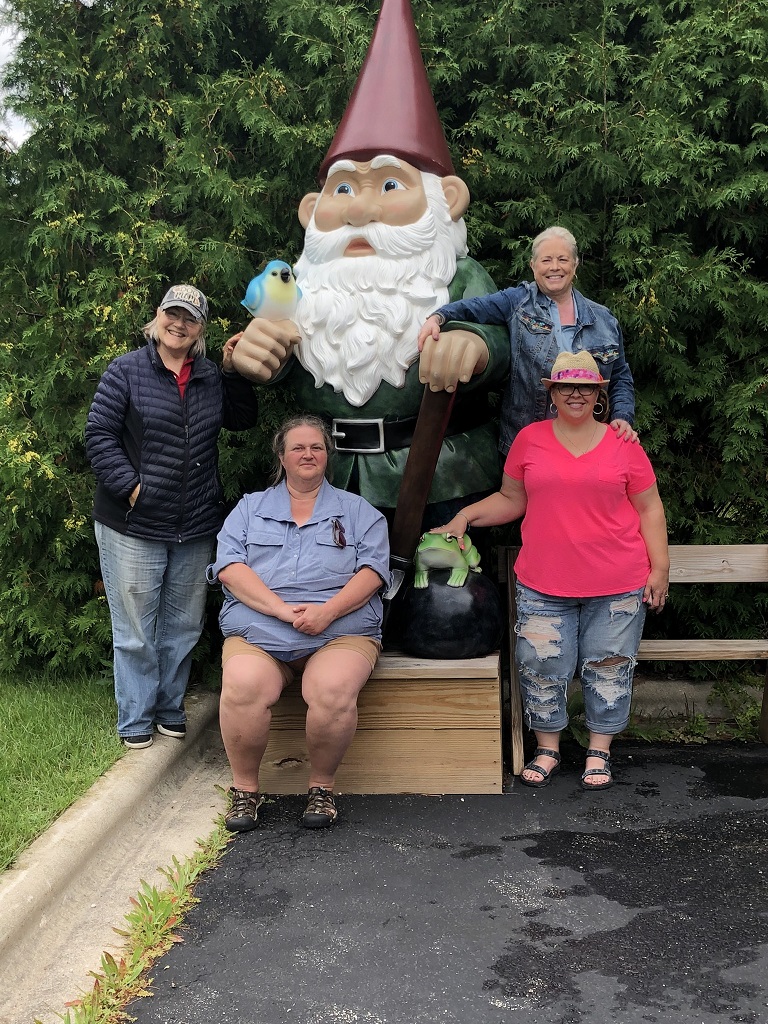 Four women posing with a giant gnome statue.