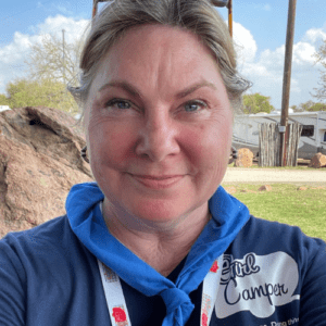 Lisa Dempsey is a women wearing a blue tshirt with aGirl Camper logo and bandana.  There are RVs in the background.