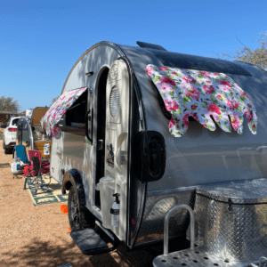 A Silver TAB teardrop style trailer is show with pink and red flowered curtains.  This was at how to start camping like a girl event Camporee