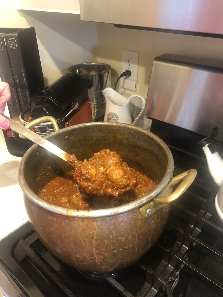 A big pot of red meat sauce with meatballs.