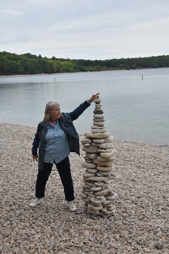 A woman touching the top of a 5-foot rock cairn on Schoolhouse Beach, Washington Island.