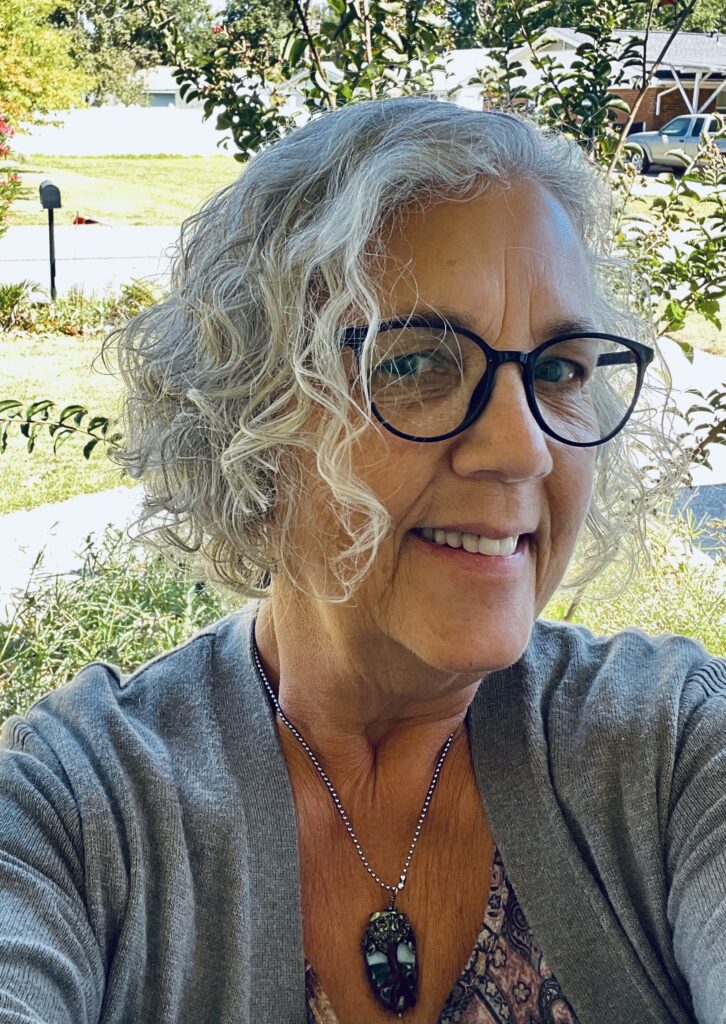 Smiling woman with curly silver hair and glasses.