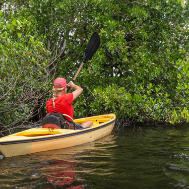 A woman with blond hair and wearing a red had and shirt is canoeing in a yellow boat