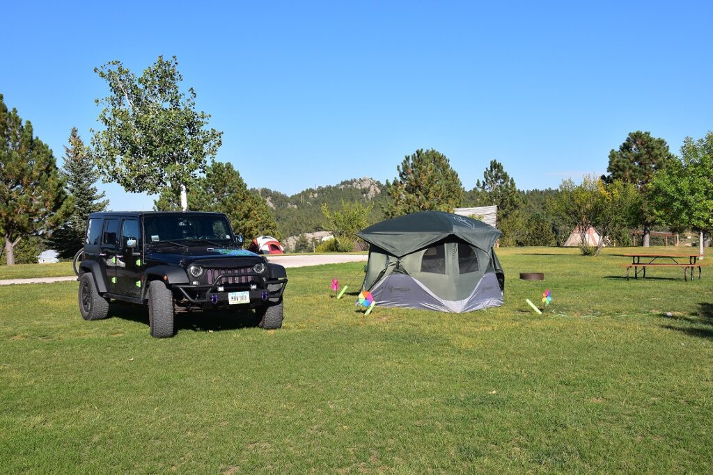 Jeep Wrangler and small green hub tent in a campground.