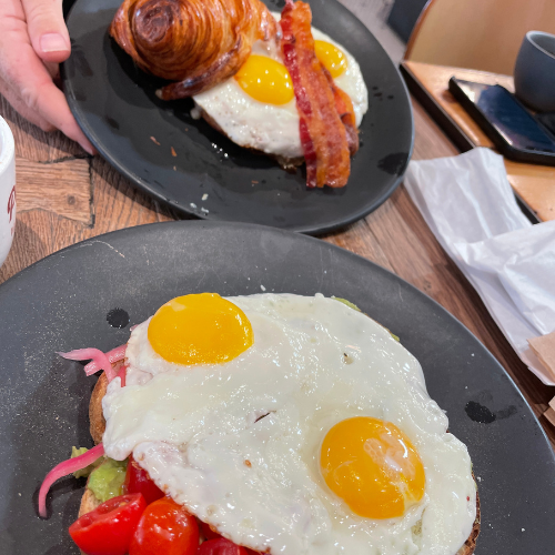 Two eggs over easy on top of toast spread with fresh avacado and tomatos.