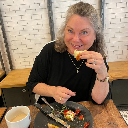 Lisa Dempsey a woman in a black shirt sits eating breakfast and drinking a coffee at La Panadaria in San Antonio