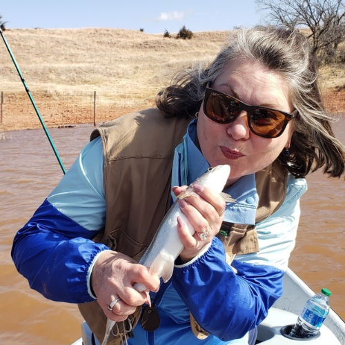 Lisa Dempsey in a blue jacket on a boat kissing a fish