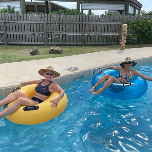 Two women floating in yellow intertubes on a lazy river wearing hats