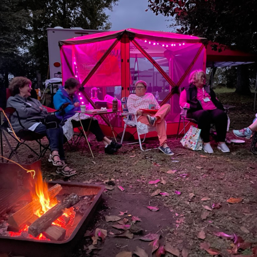 A tent lit up with pink lights and a group of ladies sitting around a campfire