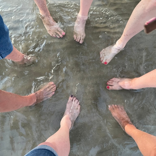 A group of ladies feet in the water as the waves come across the shoreline of Galveston Island