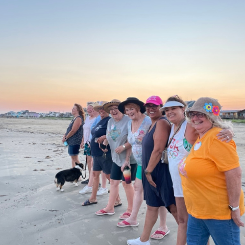 A group of women are lined up along the shoreline of a beach watching the sunset