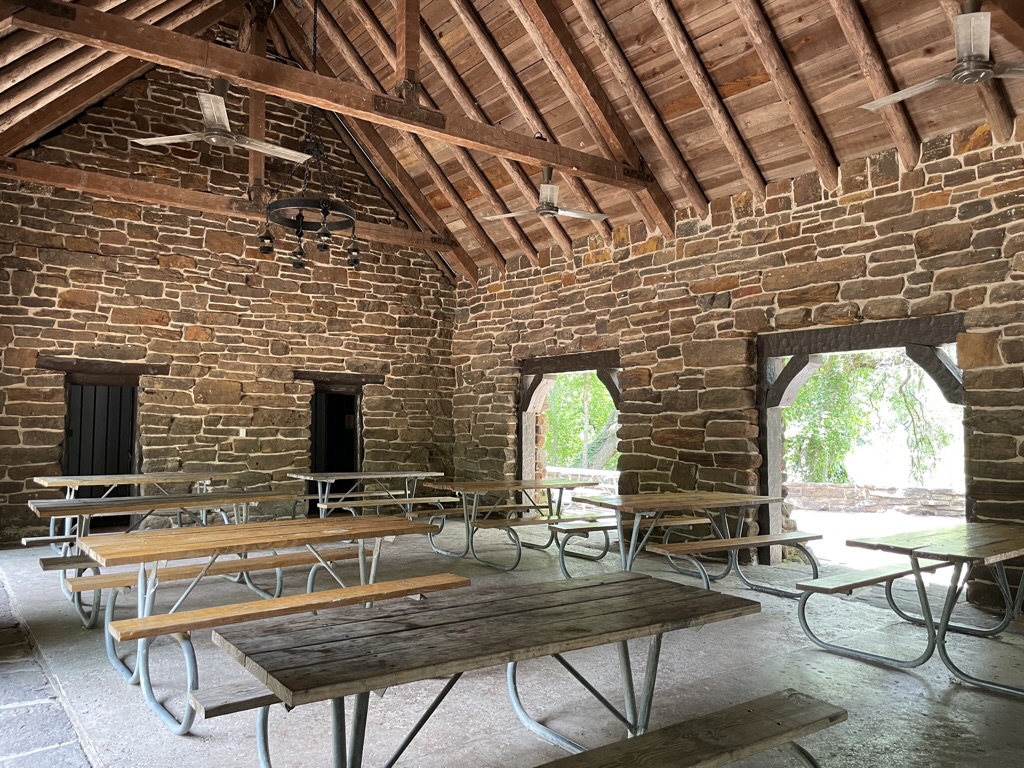 A stone and log building with large arched openings filled with picnic tables overlooks the San Marcos River built in Palmetto State Park by the Civilian Conservation Corps.