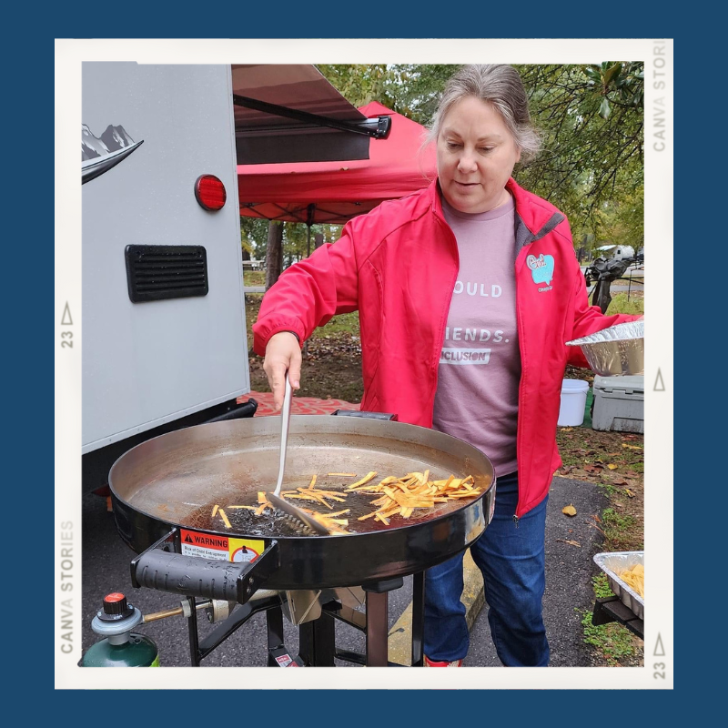 Lisa Dempsey in a red jacket standing in from of her trailer using a tall Firedic cooker to fry tortilla strips.