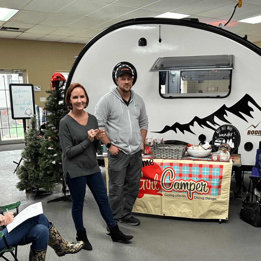 PJ Buerger and service manager Cody from Princess Craft RV in front of a Girl Camper banner that is hanging from a table filled with gifts and swag.