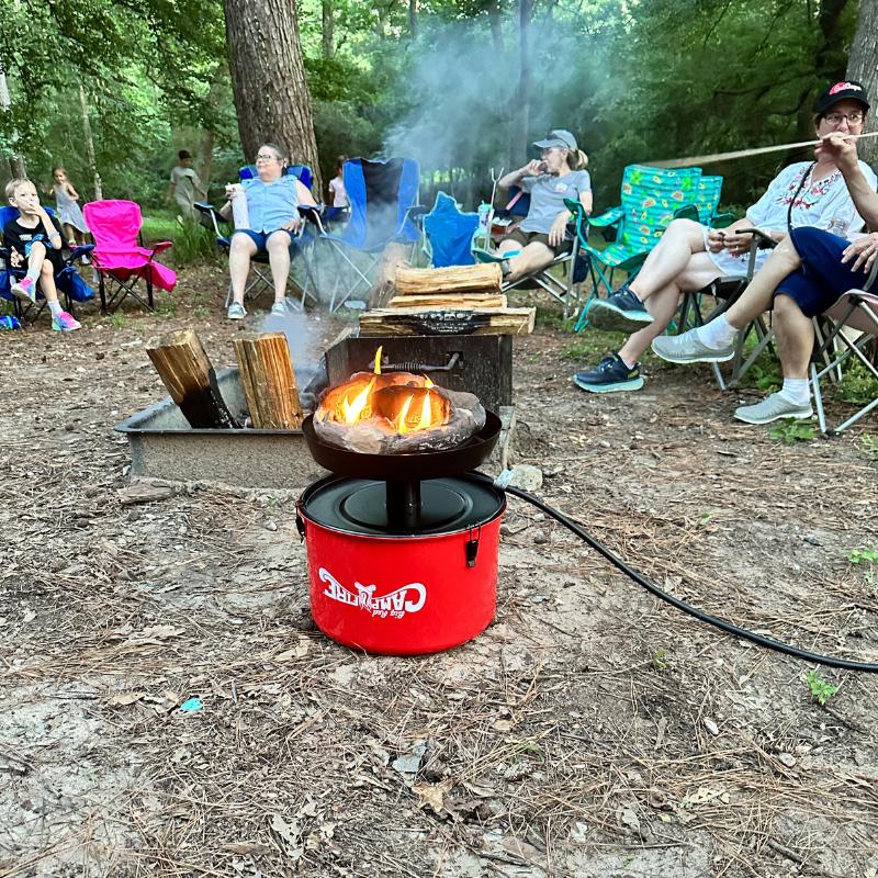 A group of Girl Campers at an event sit around the Camco Big Red Campfire.