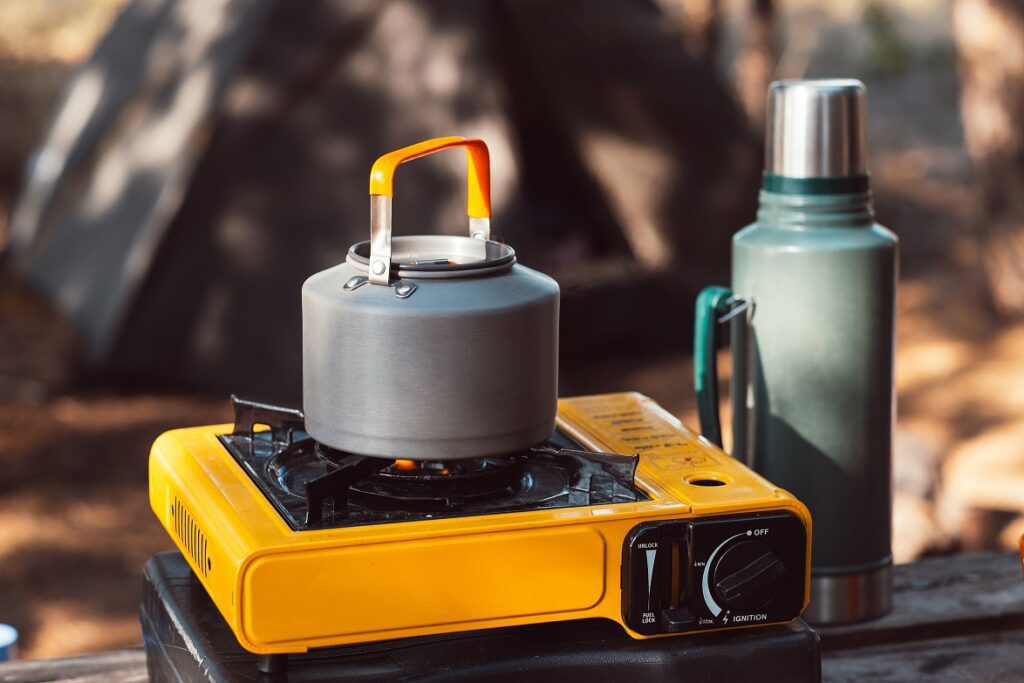 A yellow single-burner butane stove with a kettle and a thermos.